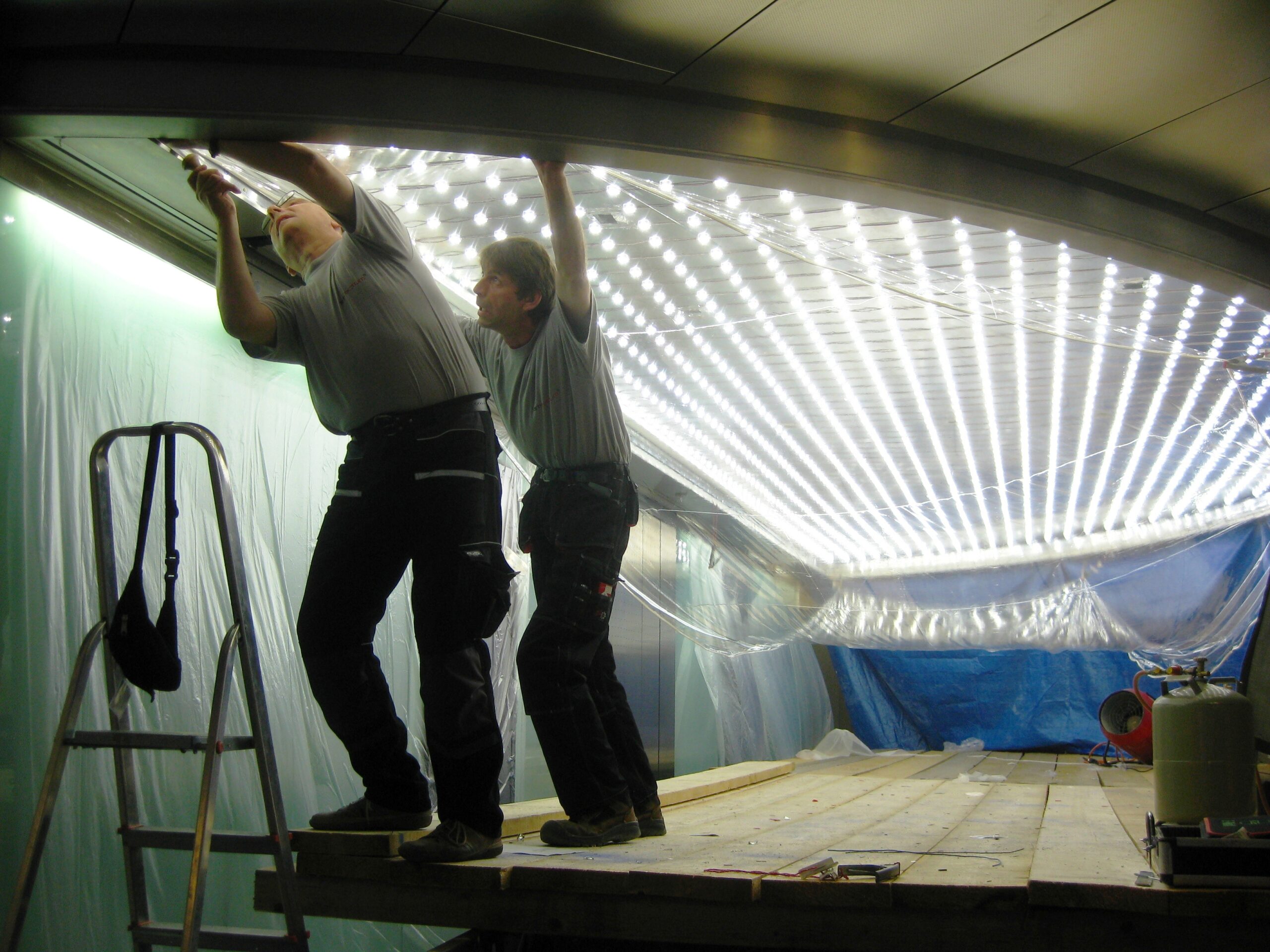 Zwei Monteure arbeiten am Rand der Lichtdecke auf einer Arbeitsplattform