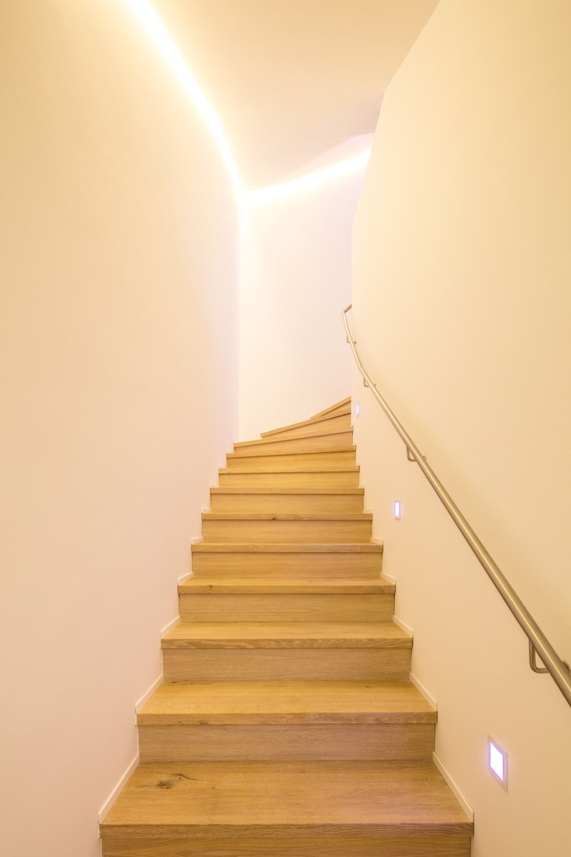 Treppenraum mit Holzstufen und einer durch Lichtvoute optisch leichter wirkenden Betondecke