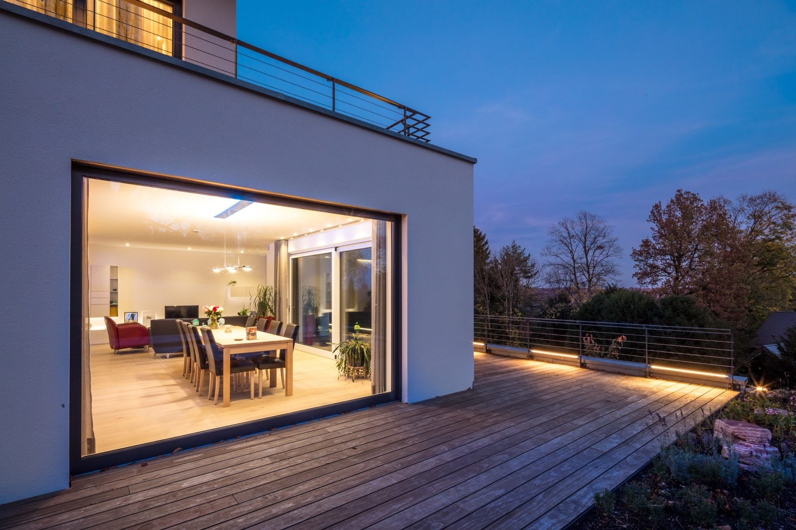 Blick von der Terrasse in den beleuchteten Wohn- und Essbereich am Abend